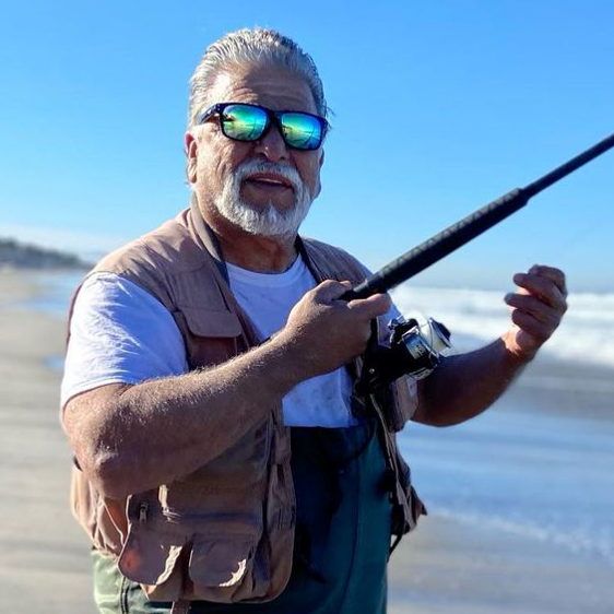 Older man wearing Sea Striker sunglasses and holding fishing pole on shore